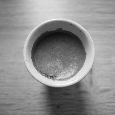 Foto einer Tasse Espresso auf einer Holzfläche, von oben fotografiert. 