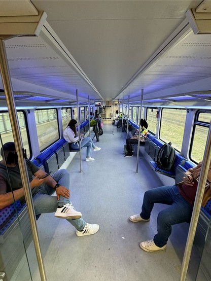 Interior of a mostly empty train car with a few passengers seated, some using smartphones, and one with a bicycle.