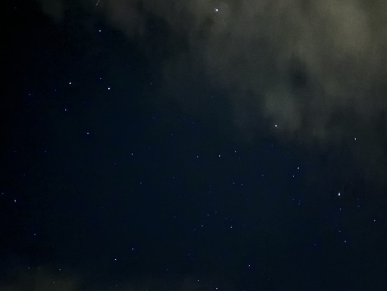 Ein was wolkenfreie Sternenhimmel scheint dunkelblau und die Sterne leuchten in einzelnen Punkten. Rechts oben schiebt sich eine Wolke ins Bild.