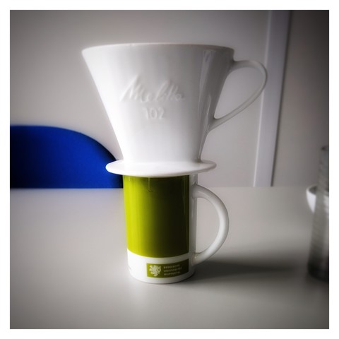 Eine Kaffeetasse mit einem Filtertütenhalter aus Porzellan drauf.

