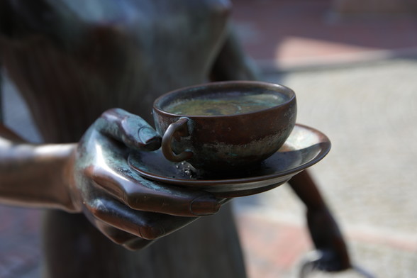 Bronzefigur trägt in der Hand eine Tasse Tee