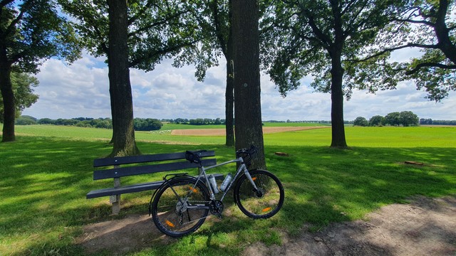 Mein Fahrrad lehnt an einer Bank unter Bäumen, im Hintergrund die sanft wellige Landschaft Süd-Limburgs.