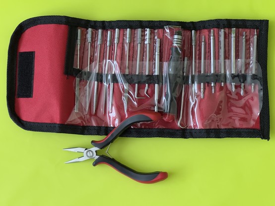 A set of small precision screwdrivers in a red and black soft tool roll with a pair of needle-nose pliers on a yellow background.