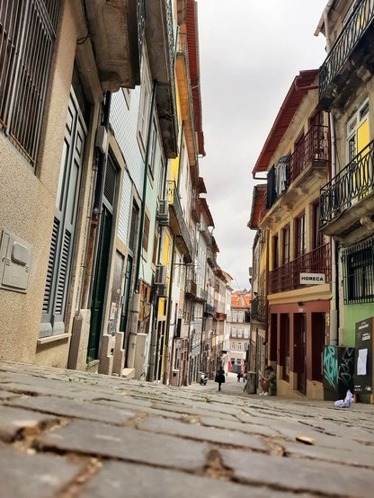 Bild einer engen, leicht abschüssigen Gasse in Porto. Im Vordergrund ist das Kopfsteinpflaster zu sehen. An beiden Seiten reihen sich bunte Häuser nebeneinander.